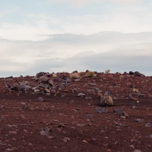 shopthietke com A barren rocky desert landscape with reddish brown soil and scattered rocks under a cloudy sky