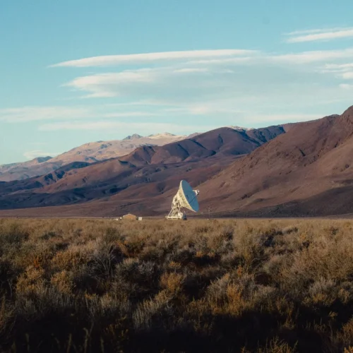 shopthietke com A desert landscape with brown mountains in the background and a large satellite dish in the middle ground surrounded by sparse desert vegetation