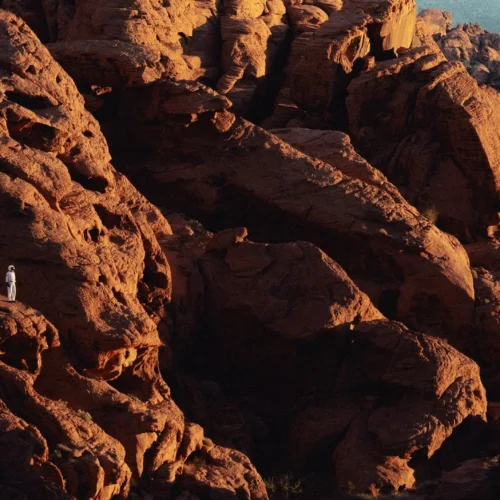 shopthietke com An astronaut in a white space suit standing on a large reddish brown rock formation in a desert landscape with rugged cliffs and mountains in the background