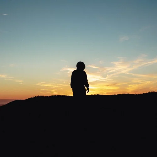 shopthietke com Silhouette of a child standing on a hill during sunset with a colorful sky and clouds in the background