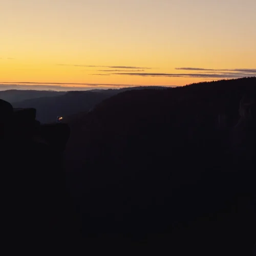 shopthietke com Silhouette of rocks and trees at sunset with a colorful sky featuring shades of yellow orange and purple over a canyon or mountain landscape